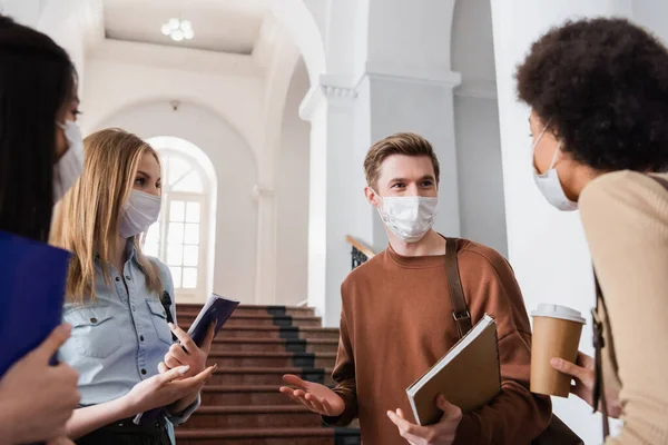 Estudiantes multiétnicos con máscaras protectoras hablando en la universidad - foto de stock