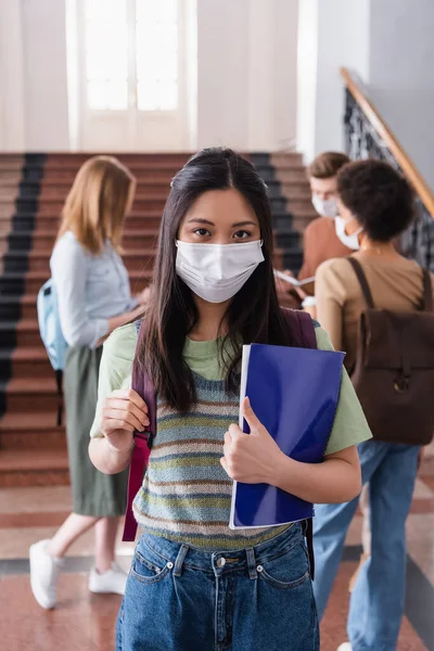 Asiática estudiante en médico máscara celebración mochila y portátil en la universidad - foto de stock