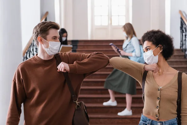 Мультиэтнические студенты в медицинских масках приветствуют с ударом локтя — стоковое фото