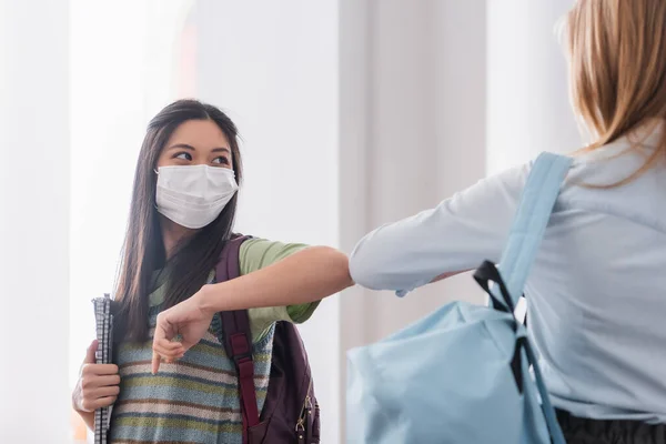 Asian student in medical mask doing elbow bump with friends in university — Stock Photo
