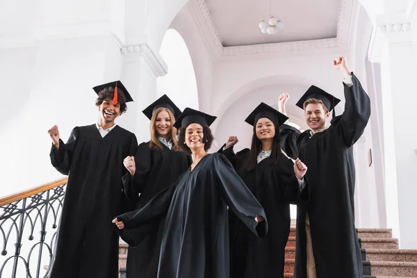 Graduados multiétnicos mostrando sí gesto en la universidad - foto de stock