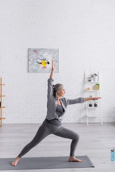 Mulher de meia idade em sportwear em pé em pose guerreira enquanto pratica ioga — Fotografia de Stock