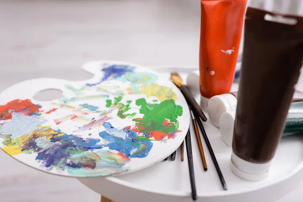Paintbrushes and palette near tubes with paint on coffee table — Stock Photo