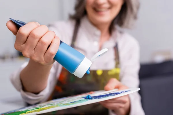 Ausgeschnittene Ansicht eines Künstlers mittleren Alters, der eine Tube mit blauer Farbe in der Nähe der Palette hält — Stockfoto