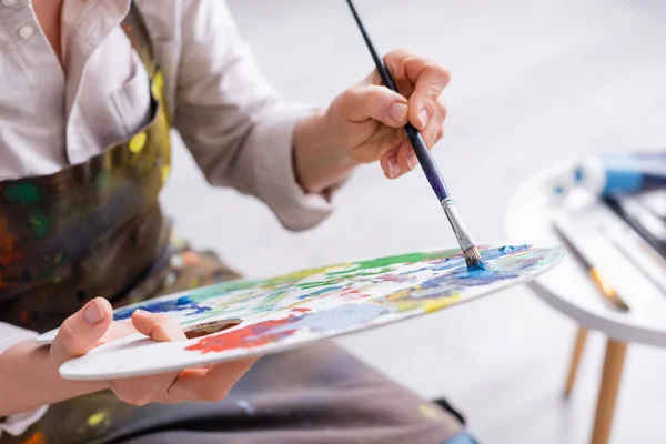 Cropped view of middle aged woman holding paintbrush and palette with colorful paints — Stock Photo