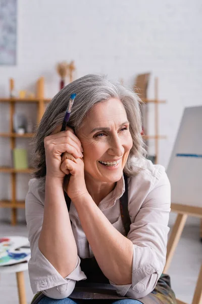 Lächelnder Maler mittleren Alters mit grauen Haaren und Pinsel — Stockfoto