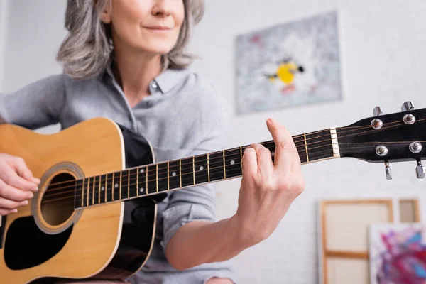 Vista parziale di una donna sorridente di mezza età che suona la chitarra acustica in salotto — Foto stock
