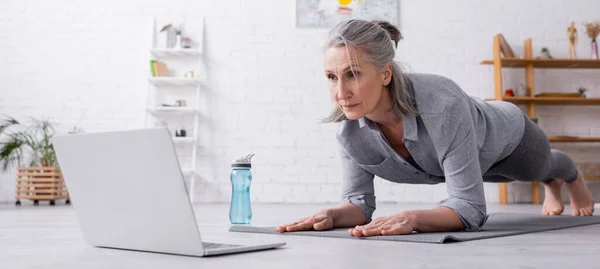 Femme mature faisant planche et regardant ordinateur portable, bannière — Photo de stock