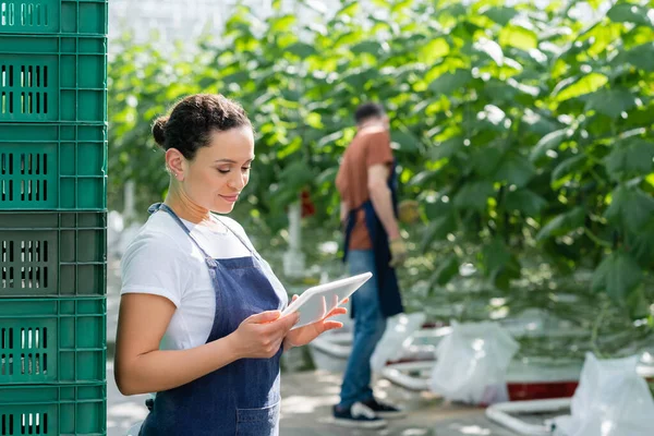 Afrikanischer amerikanischer Bauer blickt auf digitales Tablet neben Kollegen, die an verschwommenem Hintergrund arbeiten — Stockfoto