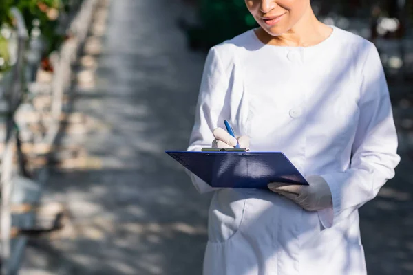 Partial view of african american quality inspector writing on clipboard in greenhouse — Stock Photo