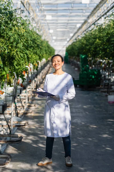 Happy african american quality inspector standing with clipboard in greenhouse — Stock Photo