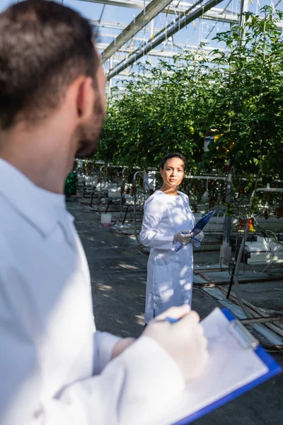 African american quality inspector looking at colleague with clipboard on blurred foreground — Stock Photo