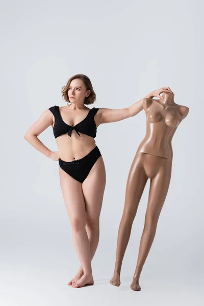 Full length of overweight and barefoot young woman posing with plastic mannequin on white — Stock Photo