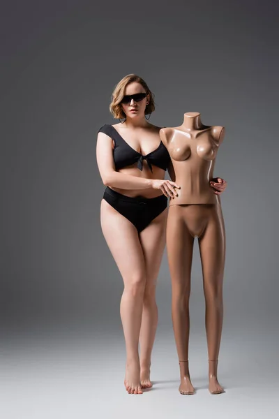 Full length of overweight woman in swimsuit and sunglasses posing with plastic mannequin on grey — Stock Photo