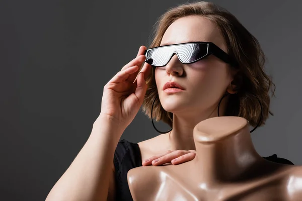Надмірна вага молода жінка регулює сонцезахисні окуляри і позує з пластиковим манекеном ізольовано на сірому — стокове фото