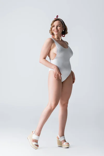 Full length of happy overweight young woman in swimwear and earrings posing on white — Stock Photo