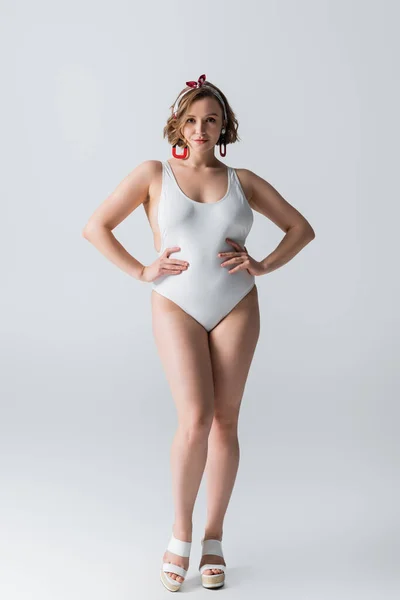 Pleine longueur de la jeune femme en surpoids en maillot de bain posant avec les mains sur les hanches sur blanc — Photo de stock