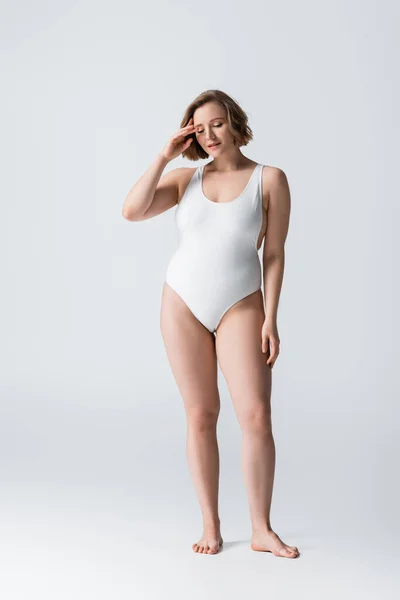 Full length of pensive overweight woman in swimsuit standing on white — Stock Photo