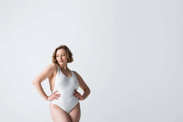 Jovem mulher com sobrepeso em roupa de banho posando com as mãos sobre os quadris isolados em branco — Fotografia de Stock