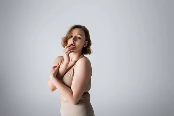 Übergewichtige junge Frau in Unterwäsche posiert auf grau — Stockfoto