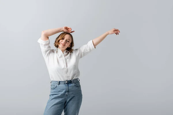 Femme en surpoids et heureuse en chemise blanche posant avec les mains au-dessus de la tête isolée sur gris — Photo de stock