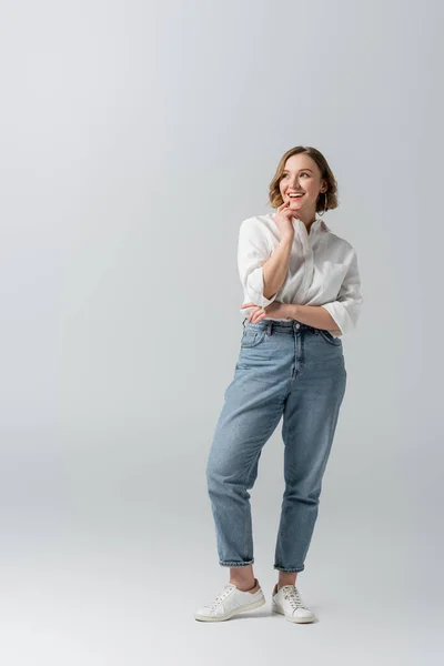 Piena lunghezza di felice donna in sovrappeso in jeans in posa su grigio — Foto stock