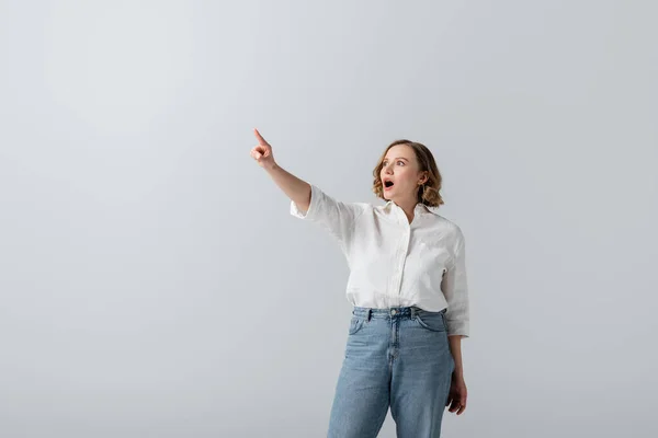 Femme en surpoids et choquée en chemise blanche pointant avec le doigt isolé sur gris — Photo de stock