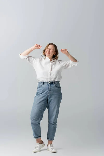 Full length of pleased overweight woman in jeans celebrating on grey — Stock Photo