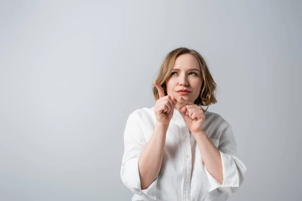 Curiosa mujer con sobrepeso en camisa blanca apuntando con los dedos aislados en gris - foto de stock