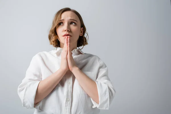 Giovane donna sovrappeso in camicia bianca con le mani in preghiera isolate sul grigio — Foto stock