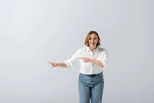 Mujer feliz con sobrepeso en jeans señalando con los dedos aislados en gris - foto de stock