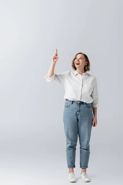 Volle Länge der glücklichen übergewichtigen Frau in Jeans, die mit dem Finger auf grau zeigt — Stockfoto