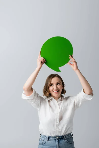 Allegra giovane donna in camicia bianca tenuta verde discorso bolla sopra la testa isolato su grigio — Foto stock