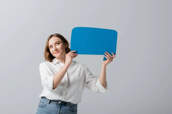 Mujer con sobrepeso complacido en camisa blanca sosteniendo burbuja de habla azul aislada en gris - foto de stock