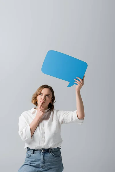 Pensive overweight woman in white shirt holding blue speech bubble isolated on grey — Stock Photo