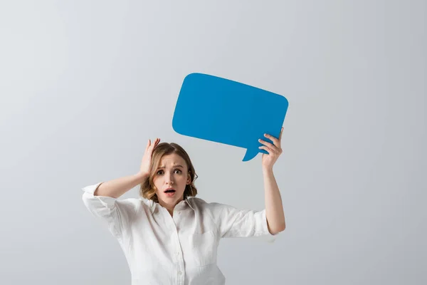 Shocked overweight woman in white shirt holding blue speech bubble isolated on grey — Stock Photo