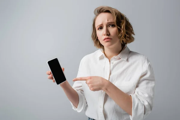 Young overweight woman pointing at smartphone with blank screen isolated on grey — Stock Photo