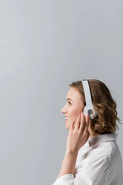 Вид збоку щасливої жінки плюс розмір в бездротових навушниках слухати музику ізольовано на сірому — стокове фото