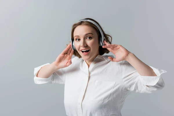 Здивована жінка плюс розмір в бездротових навушниках слухає музику ізольовано на сірому — стокове фото