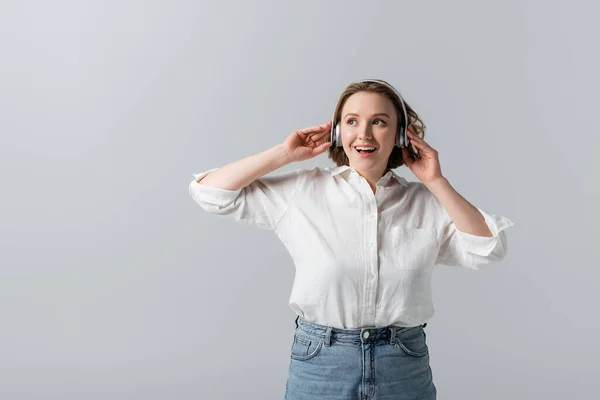 Excitada mujer de tamaño grande en auriculares inalámbricos escuchando música aislada en gris - foto de stock