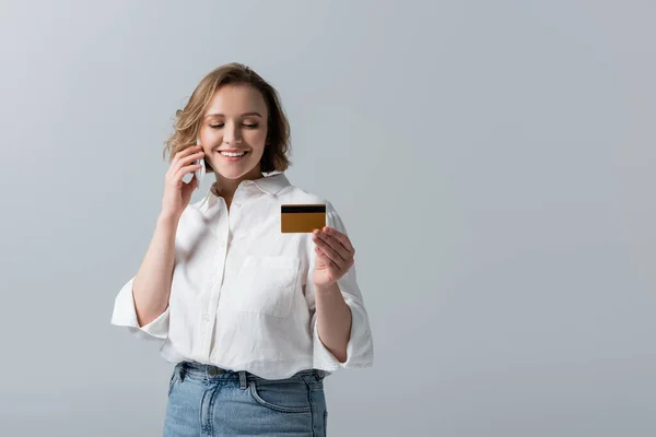 Vista parcial de la mujer de talla grande sosteniendo la tarjeta de crédito y hablando en el teléfono inteligente aislado en gris - foto de stock