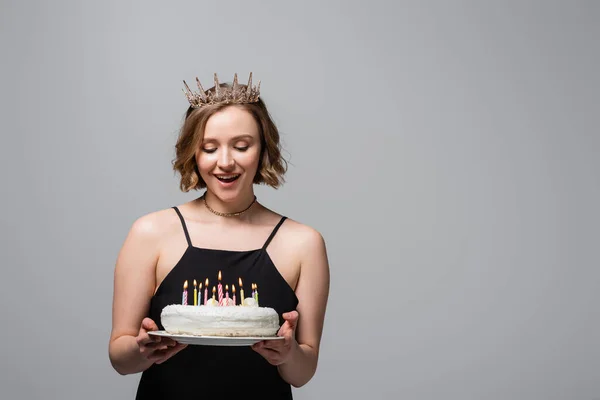 Happy plus size woman in slip dress and crown holding birthday cake isolated on grey — Stock Photo