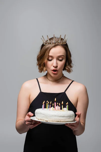 Sorpreso plus size donna in abito antiscivolo e corona tenendo torta di compleanno isolato su grigio — Foto stock