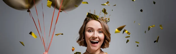 Happy plus size woman in crown holding balloons near confetti on grey, banner — Stock Photo