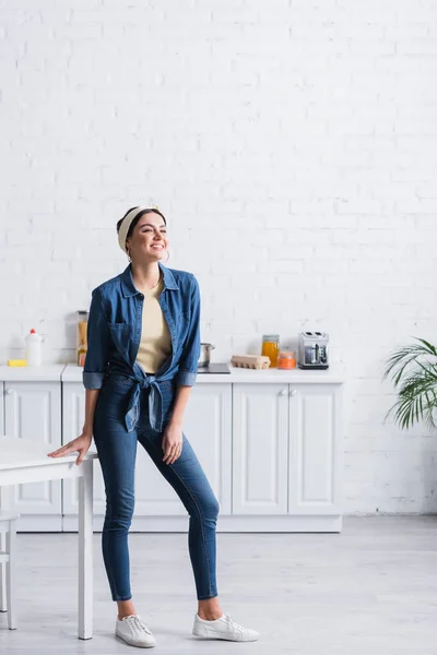 Alegre dona de casa de pé perto da mesa no cozinha — Fotografia de Stock