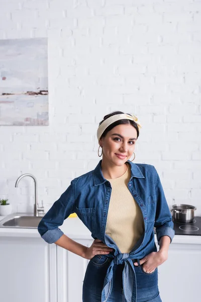 Femme au foyer avec la main sur la hanche souriant à la caméra dans la cuisine — Photo de stock