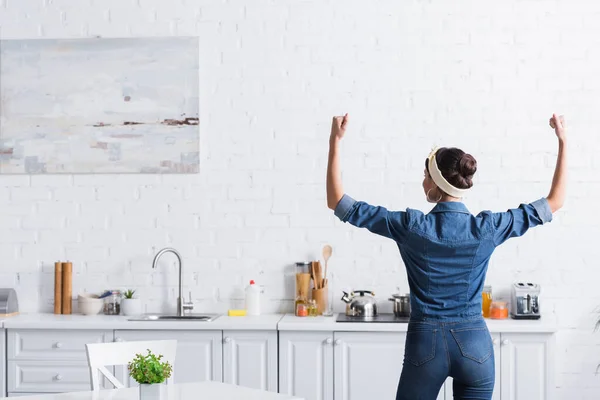 Back view of housewife in denim shirt showing muscles in kitchen — Stock Photo