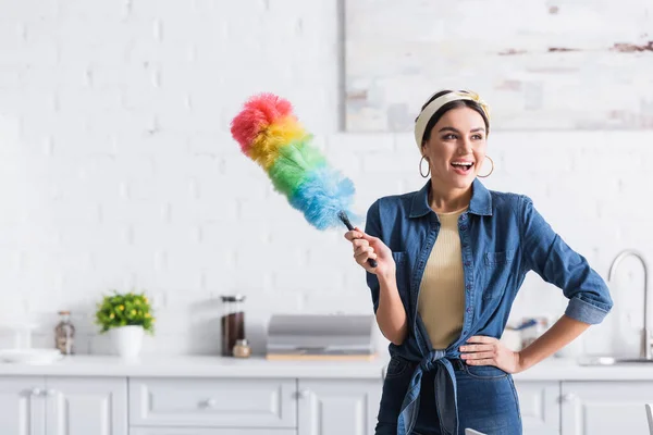 Feliz ama de casa sosteniendo polvo cepillo en cocina - foto de stock
