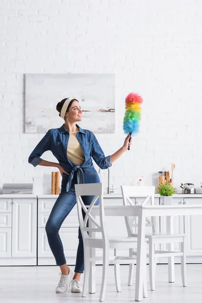 Улыбающаяся женщина в повязке держит пыльную щетку на кухне — стоковое фото