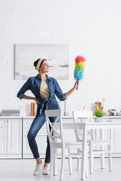 Mulher sorridente na cabeça segurando escova de poeira na cozinha — Fotografia de Stock